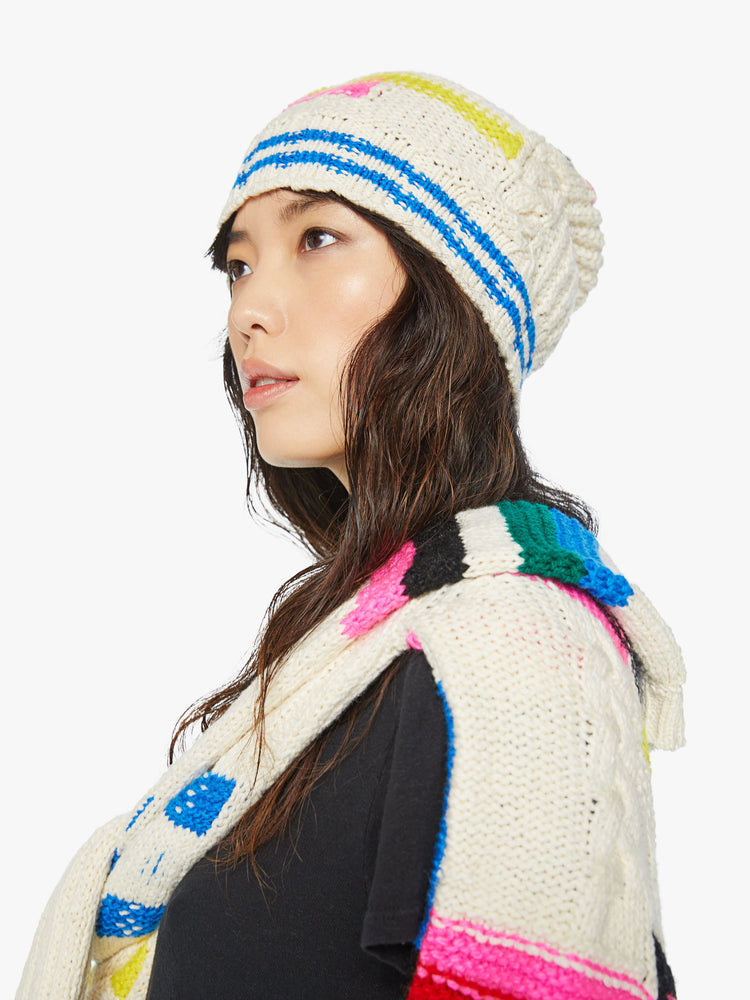 Side angle view a knit beanie with a ribbed hem and a snug fit in an off-white with colorful stripes, checks and cable knits details.