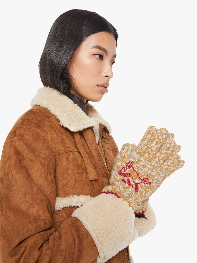 On model view of a woman in marled golden-yellow and white with red embroidered horses and trim gloves.
