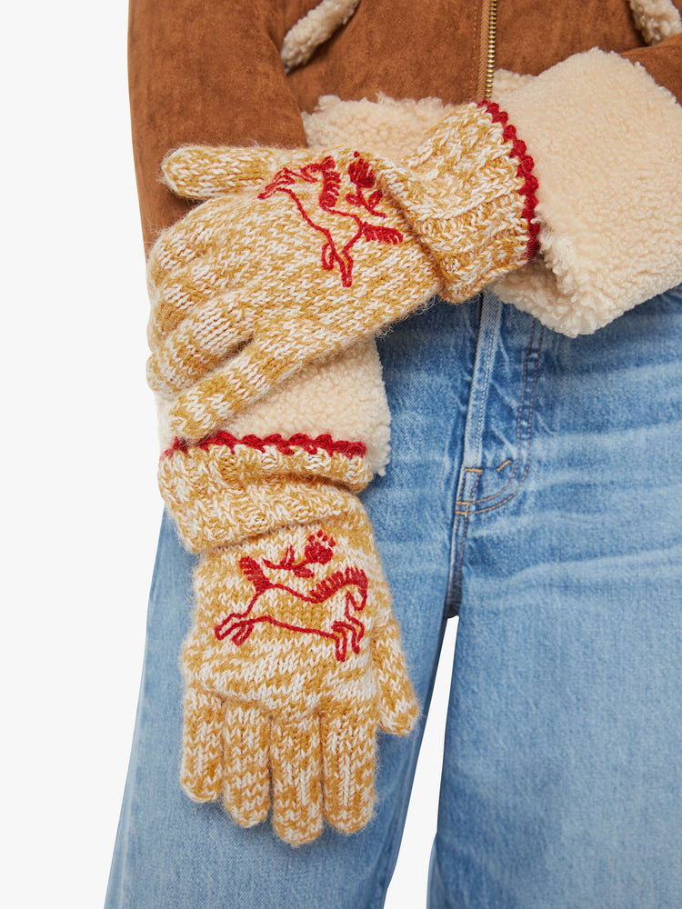 On model view of a woman in marled golden-yellow and white with red embroidered horses and trim gloves.
