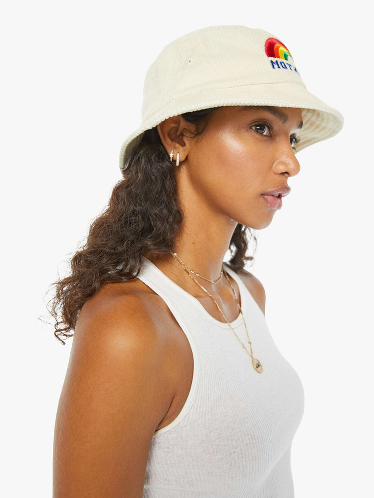 Side view of a woman in an off-white corduroy bucket hat with a rainbow graphic embroidered on the front.
