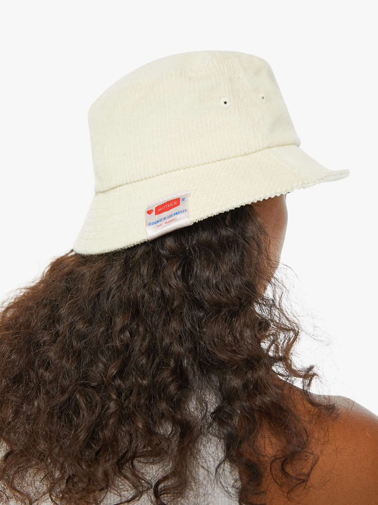 Back view of a woman in an off-white corduroy bucket hat with a MOTHER tag on the back.