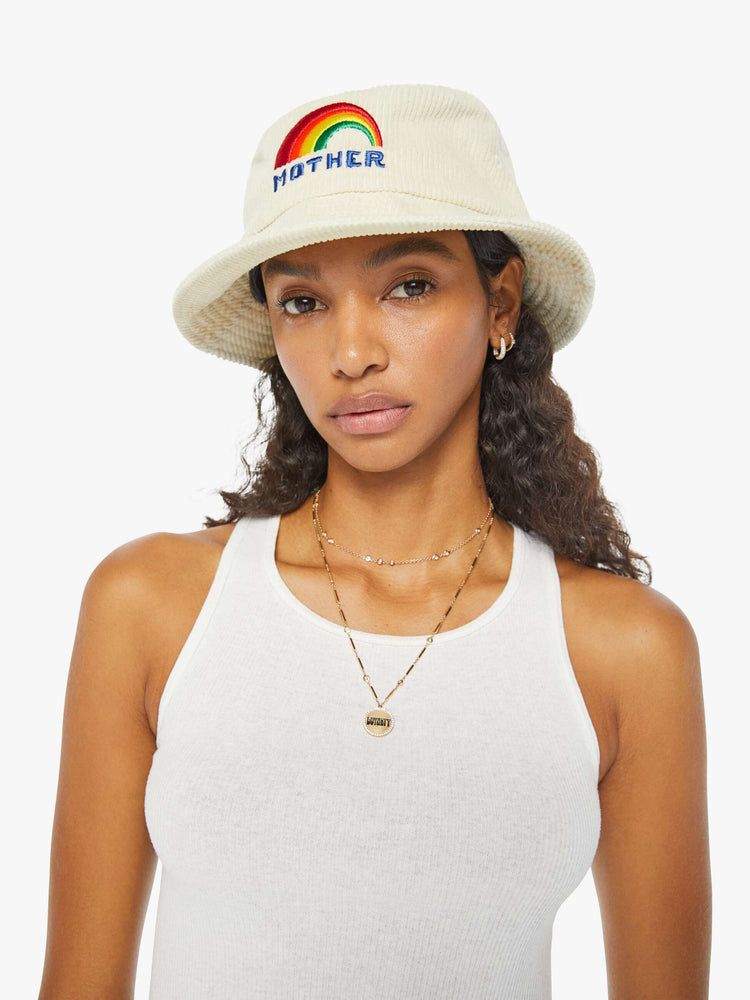 Front view of a woman in an off-white corduroy bucket hat with a rainbow graphic embroidered on the front.
