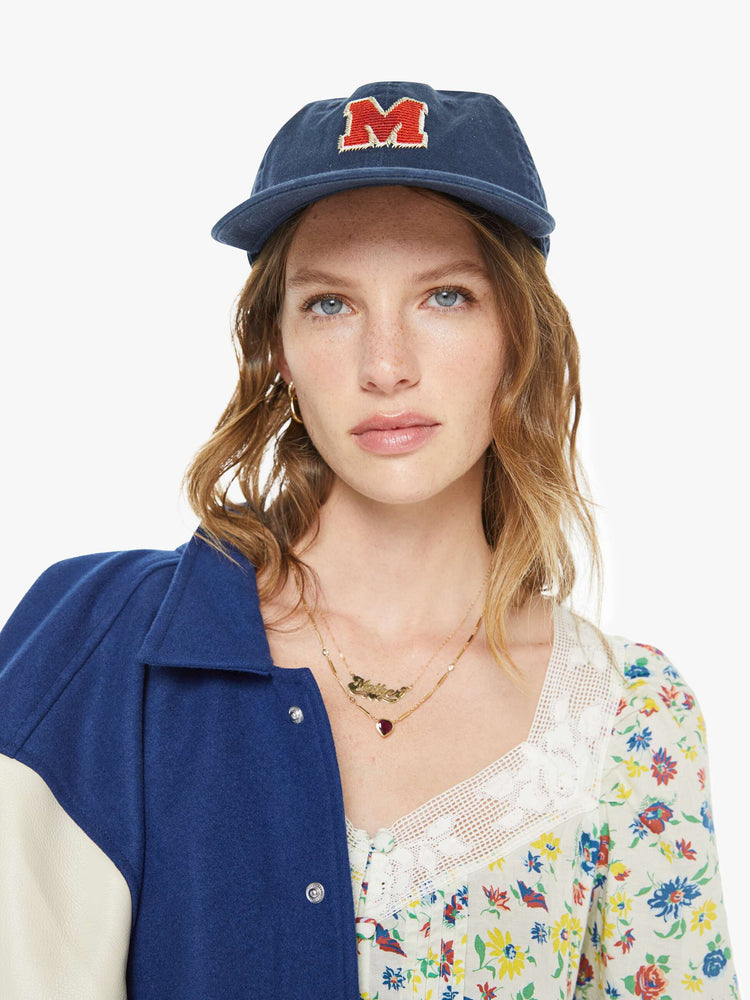 Front view on model of a dad hat designed in navy 100% cotton with an M embroidered in red and white on the front.