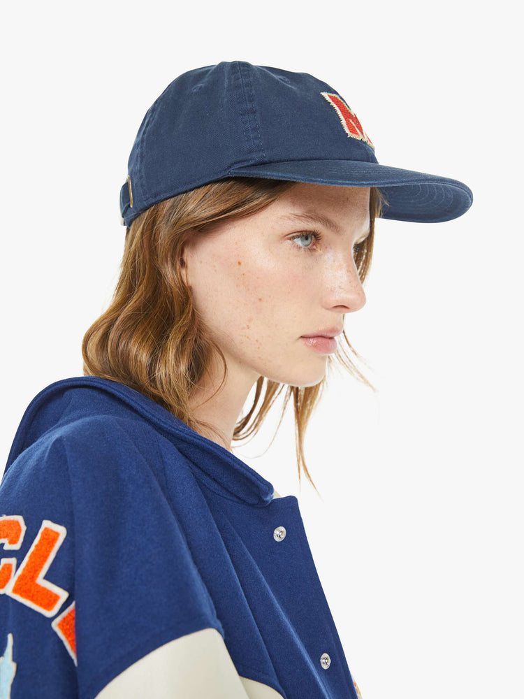 Side view on a model of a dad hat designed in navy 100% cotton with an M embroidered in red and white on the front.