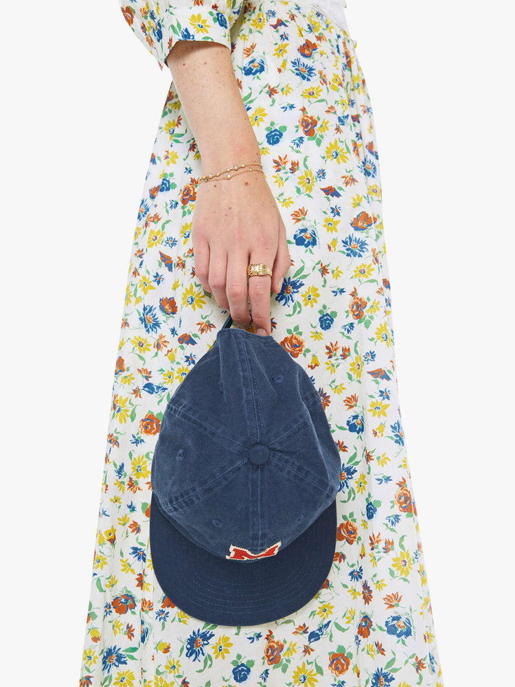 Holding model of a dad hat designed in navy 100% cotton with an M embroidered in red and white on the front.