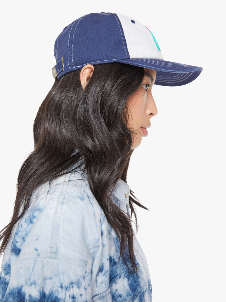 Side on model view of a woman dad hat designed in white and navy 100% cotton with white stitching and an M embroidered in teal on the front.