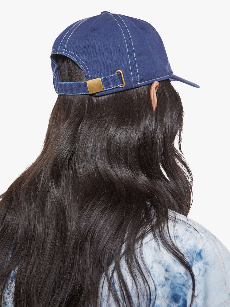 On model back view of a woman dad hat designed in white and navy 100% cotton with white stitching and an M embroidered in teal on the front.