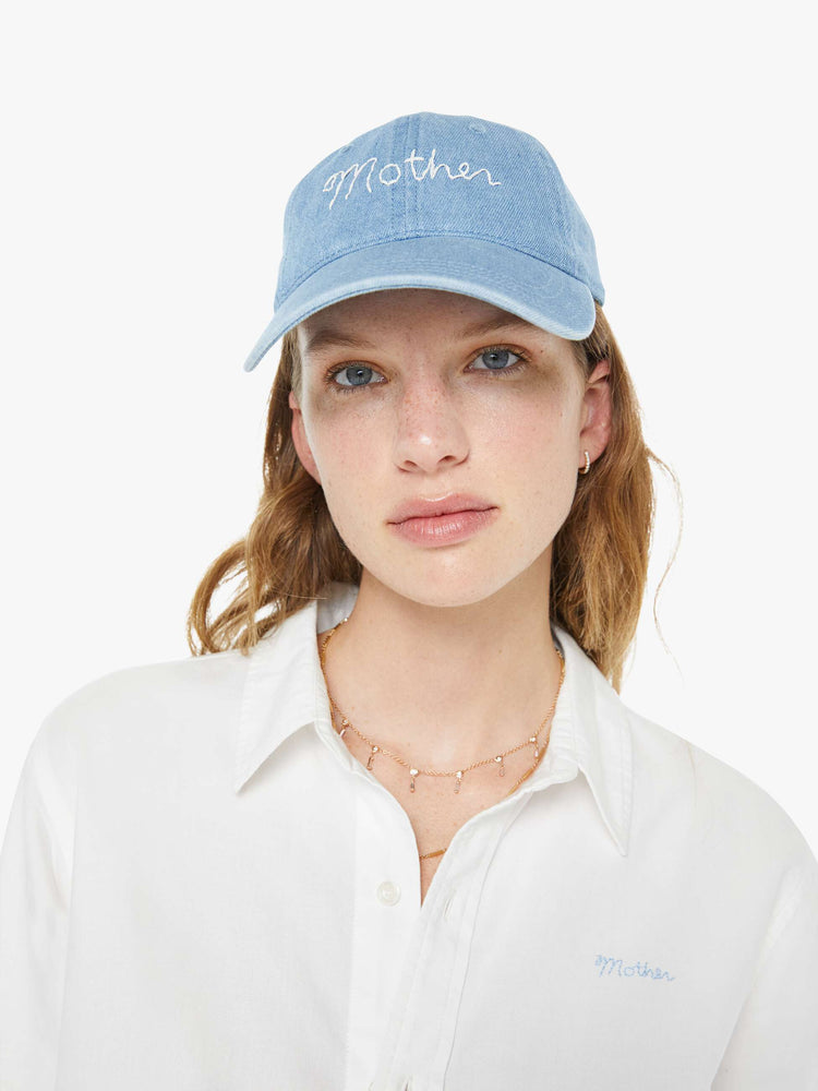 Front view of a woman in a dad hat designed in light blue denim with MOTHER's name embroidered in white cursive on the front.