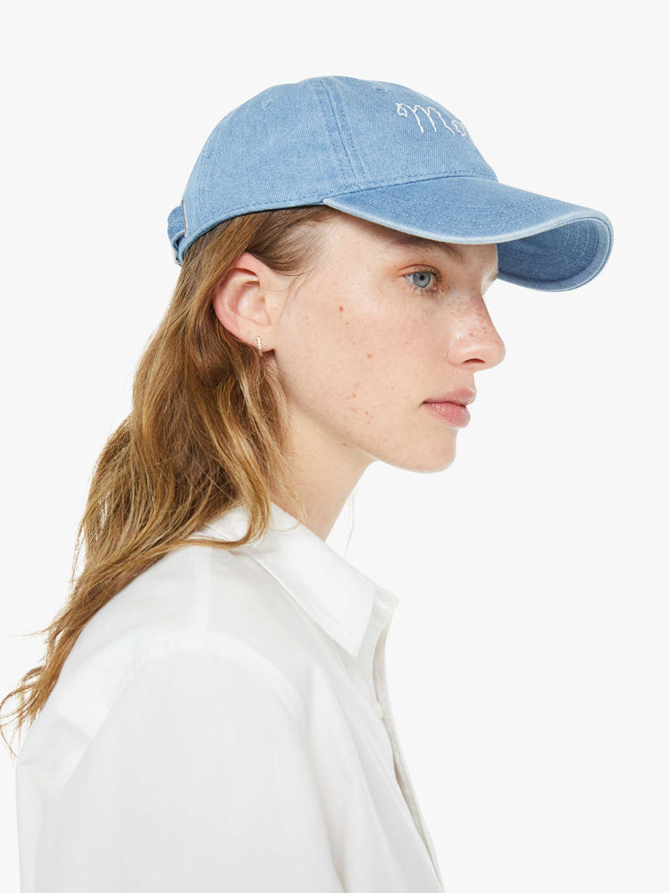 Side view of a woman in a dad hat designed in light blue denim with MOTHER's name embroidered in white cursive on the front.