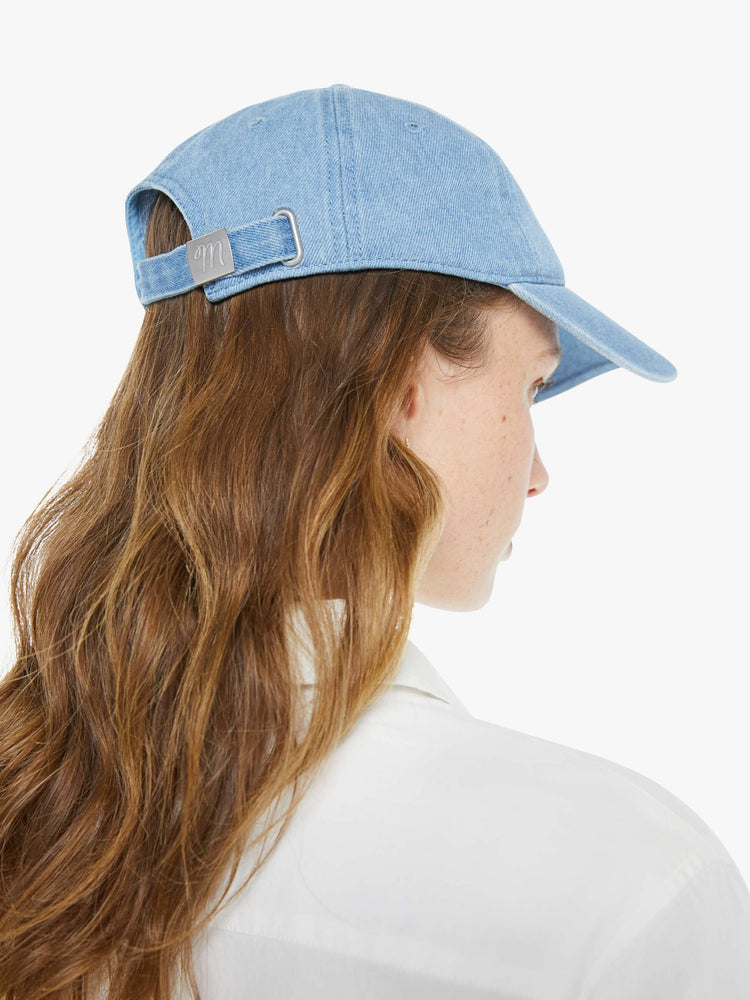 Back view of a woman in a dad hat designed in light blue denim with MOTHER's name embroidered in white cursive on the front.