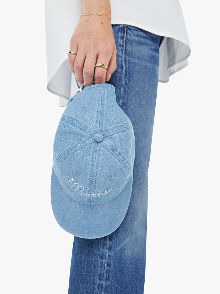 On hand view of a woman in a dad hat designed in light blue denim with MOTHER's name embroidered in white cursive on the front.
