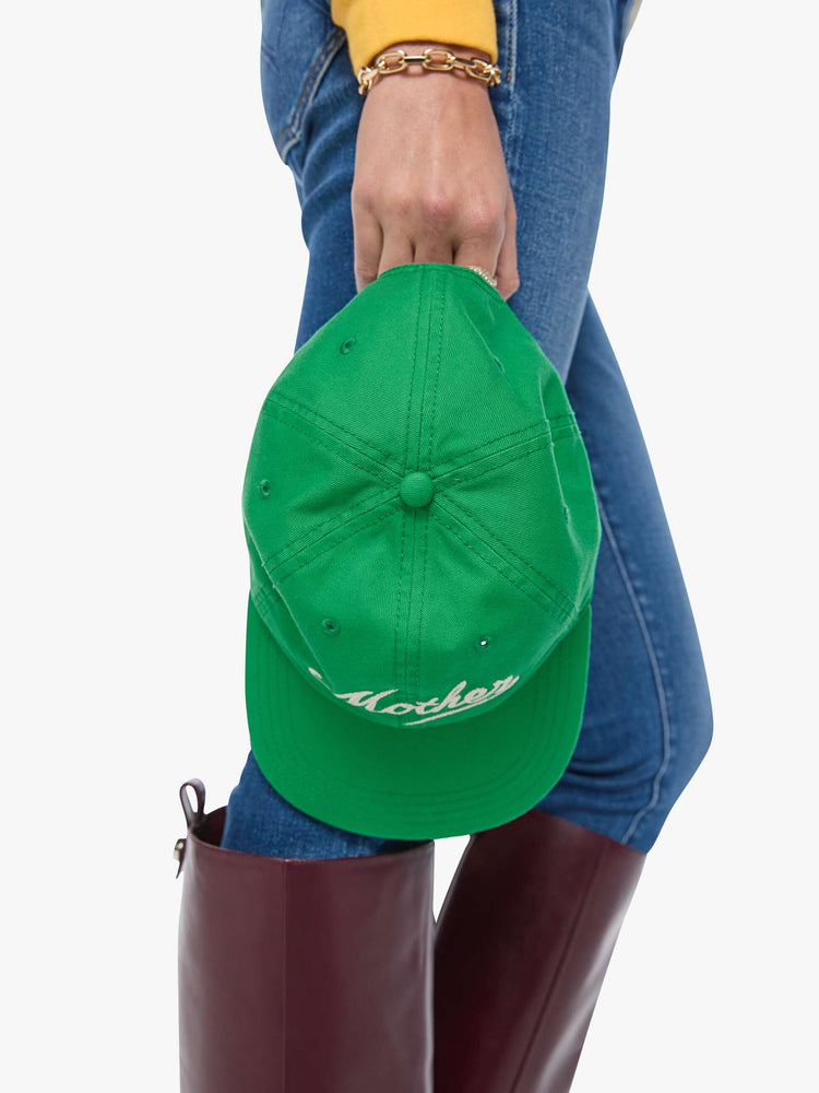 Model holding view of a woman in a dad hat designed in green 100% cotton with MOTHER's name embroidered in cream text on the front.