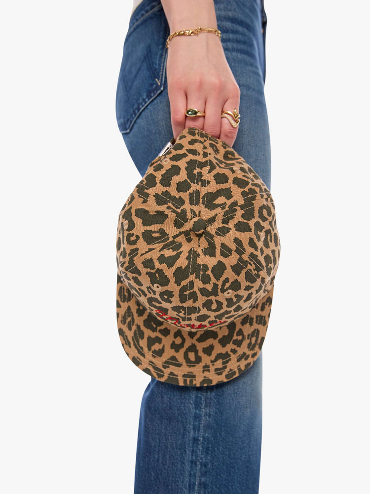 Holding view of a woman in a dad hat designed in leopard print with MOTHER's name embroidered in red cursive on the front.
