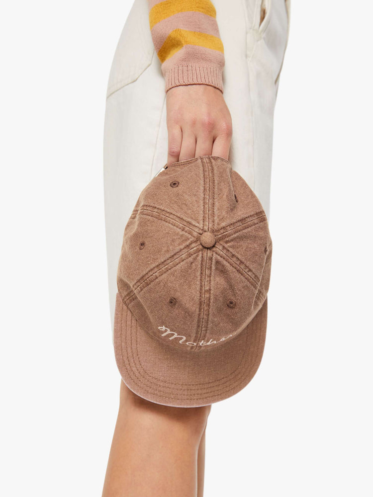 Model holding a dad hat designed in faded brown with MOTHER's name embroidered in white cursive on the front.
