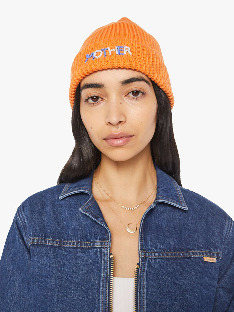 Front view of a woman in an orange with light blue and white beads ribbed beanie with a folded hem.