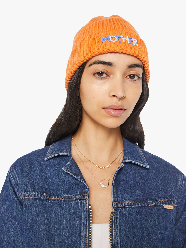 Side angle view of a woman in an orange with light blue and white beads ribbed beanie with a folded hem.