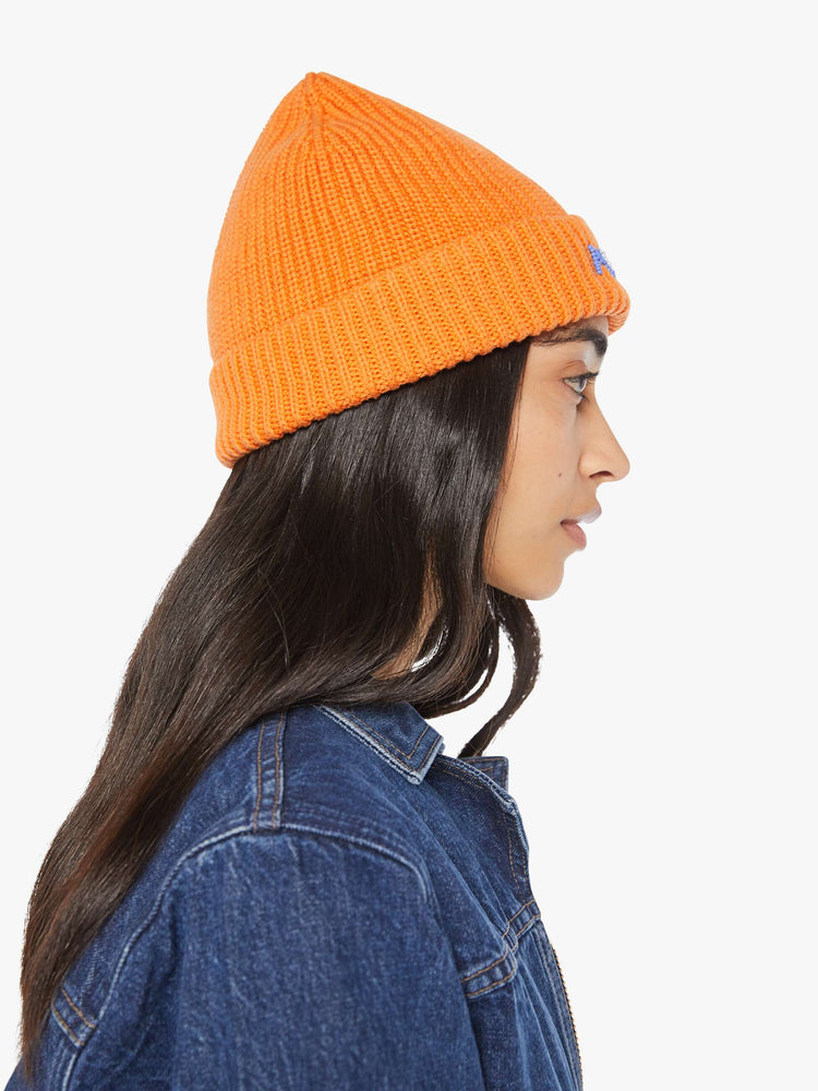 Side view of a woman in an orange with light blue and white beads ribbed beanie with a folded hem.