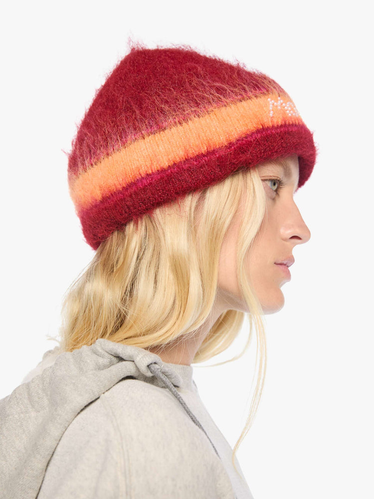 Side view of a woman in red with hot pink and orange stripes knit beanie with a folded brim and MOTHER's name in pearl beads across the front. 