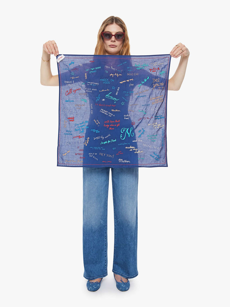 Model holding a square scarf designed to be worn around the neck, on your head or tied on a bag.