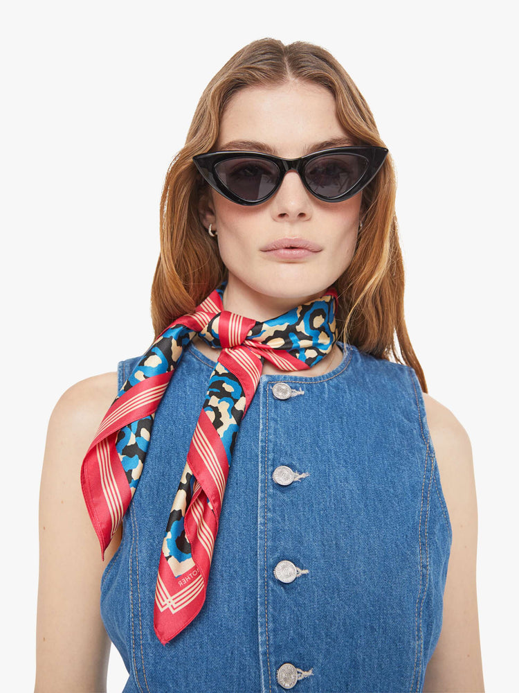 Model wearing a white, blue and black leopard print with pink and red trim square scarf.