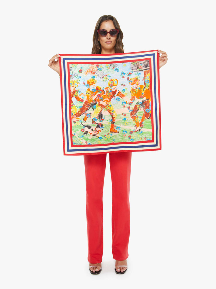 Woman holding 25" square scarf made from 100% silk with a football-inspired graphic and red, white and blue striped trim.