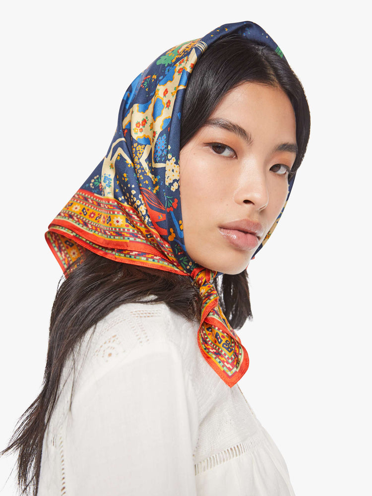 On model square scarf made from 100% silk in navy blue with a folk art-inspired horse print and orange trim.