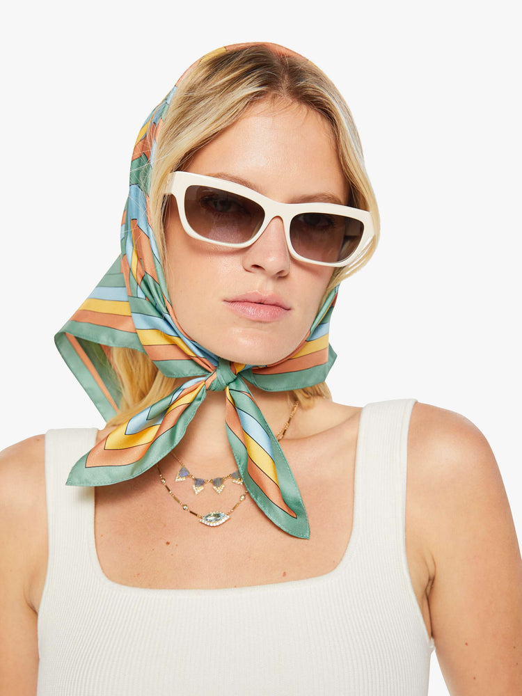On model 25-inch square scarf made from 100% silk in pastel blue, orange and yellow with a trippy sun graphic at the center.