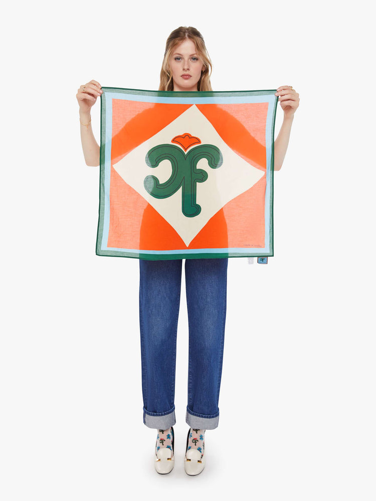 Model holding view of a red with green and blue trim square scarf can be worn as a neck tie, hair accessory or tied on a bag. 