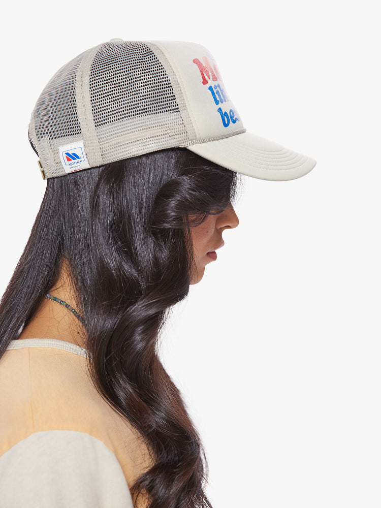 Side view woman of a vintage-inspired trucker hat designed in a light grey hue with a red and blue text graphic on the front.