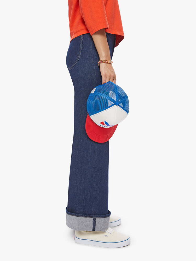 Side view of a woman holding a blue, white and red trucker hat.