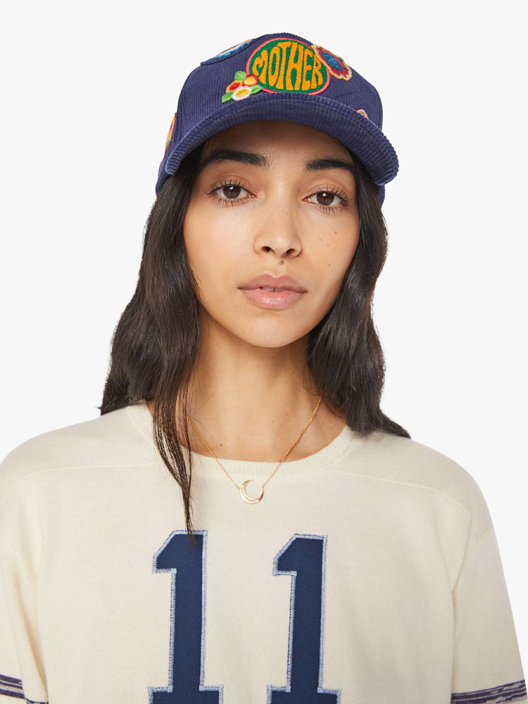 Front view of a woman in a navy corduroy hat with MOTHER's name on the front and colorful patches throughout.