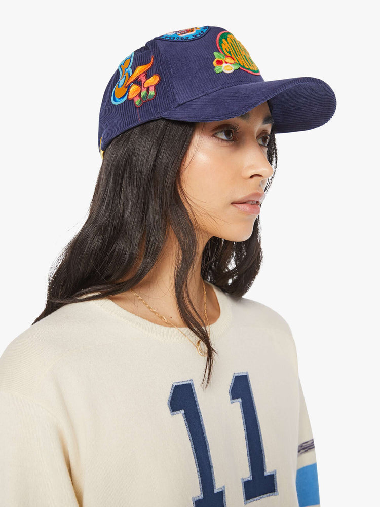 Side view of a woman in a navy corduroy hat with MOTHER's name on the front and colorful patches throughout.