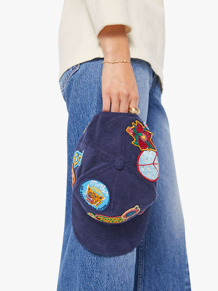 On hand view of a woman in a navy corduroy hat with MOTHER's name on the front and colorful patches throughout.