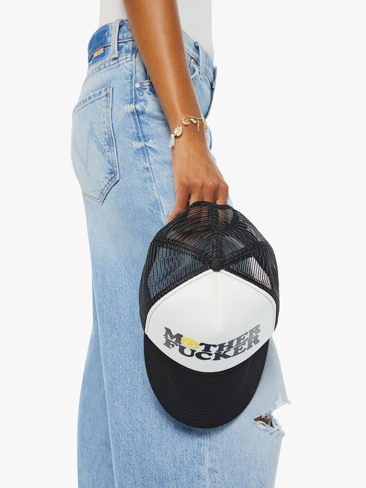 In hands view on model of a trucker hat designed in black and white with an explicit text graphic on the front.