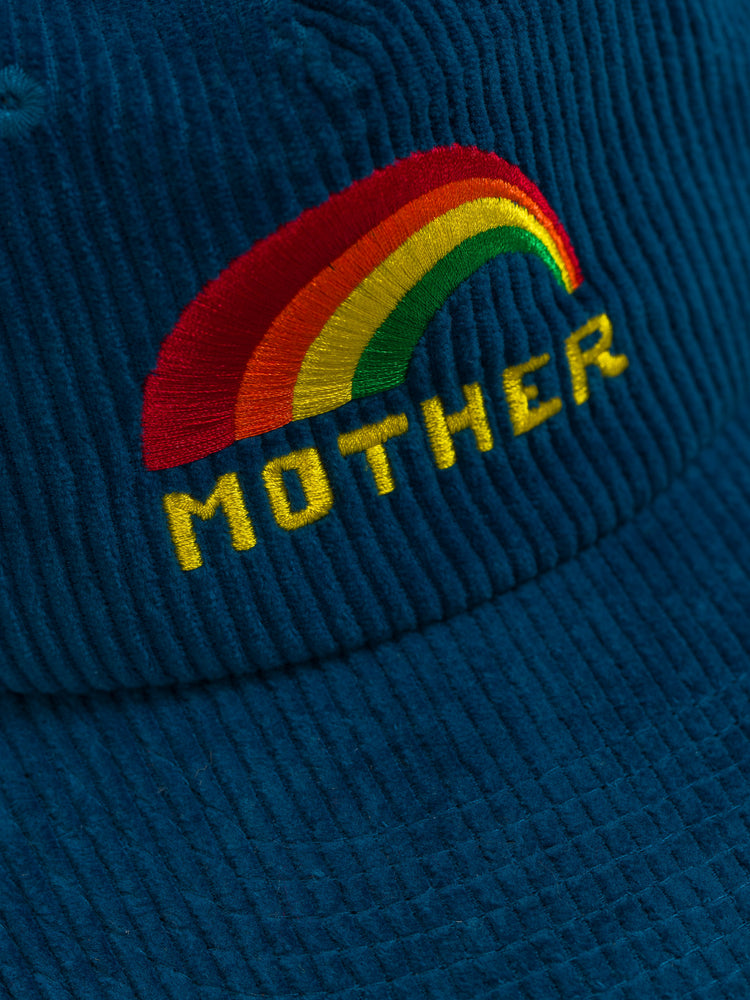 Close up view of a vintage-inspired trucker hat designed in blue corduroy and mesh with an embroidered rainbow graphic and MOTHER's name on the front.