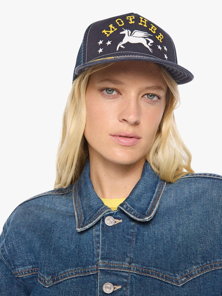 On model view in a vintage-inspired trucker hat designed in navy with a Pegasus graphic and MOTHER's name in yellow on the front.
