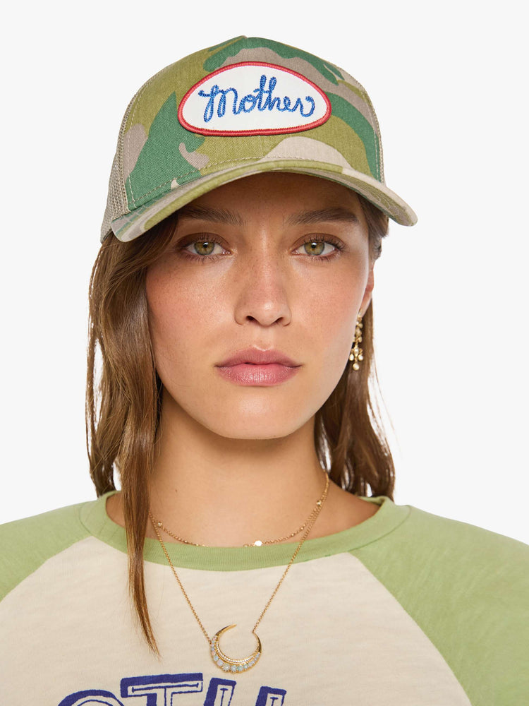 On model view of a vintage-inspired trucker hat designed in camo with an oversized white and red patch with MOTHER's name in blue on the front.