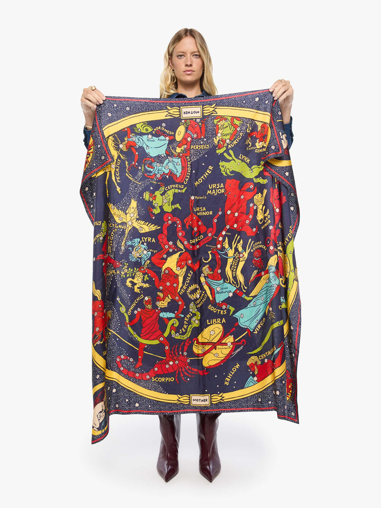 Model holding view of a woman holding a navy graphic map of cosmos oversized 46-inch square scarf can be worn around the shoulders, on the waist or tied on a bag.