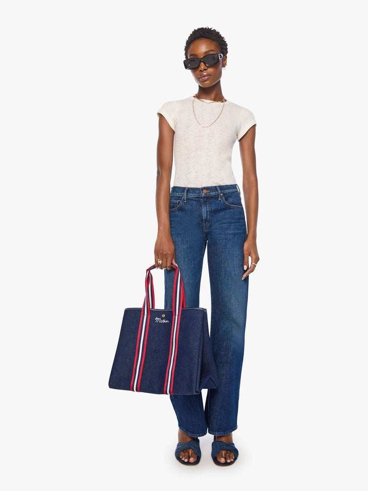 Full body  view of a dark denim with red and white trim top handles and MOTHER embroidered across the front in white. 