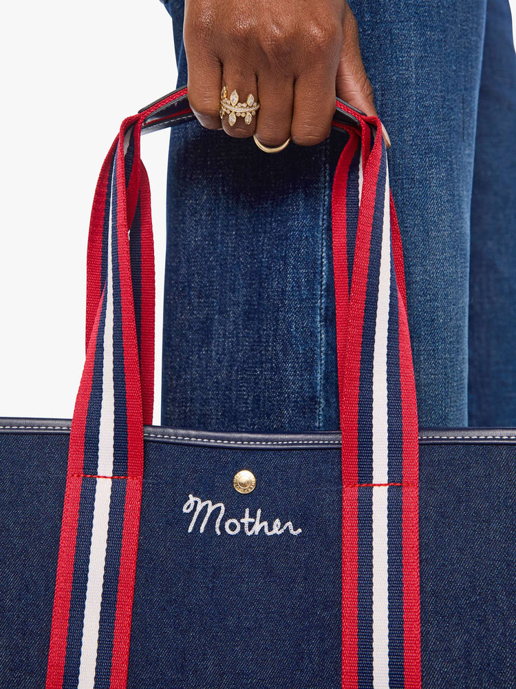 Close up  view of a dark denim with red and white trim top handles and MOTHER embroidered across the front in white. 
