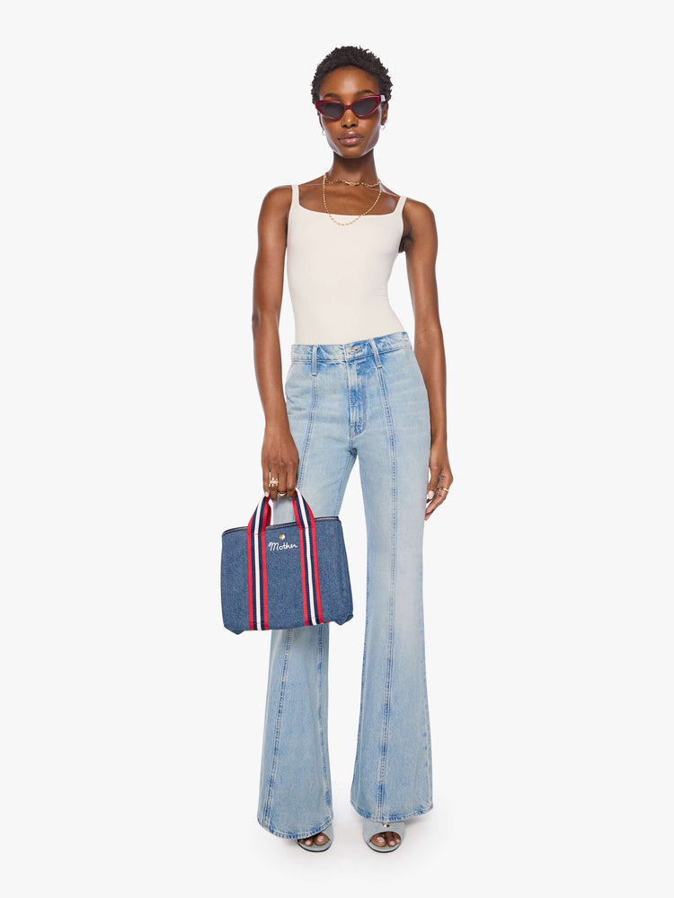 On model view of a classic blue denim with red and white trim, top handles, an optional 34-inch shoulder strap, a snap closure and MOTHER embroidered across the front in white.