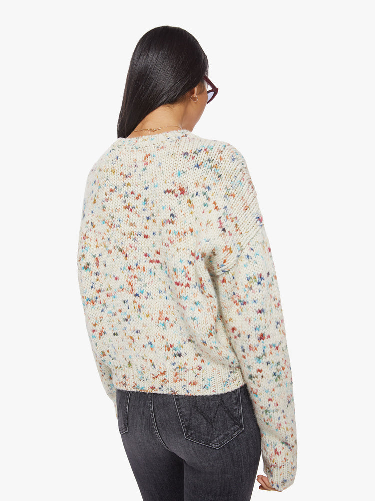 Back view of a woman crewneck sweater with drop shoulders, long roomy sleeves and a slightly cropped hem in cream with colorful speckles and text in hot pink.