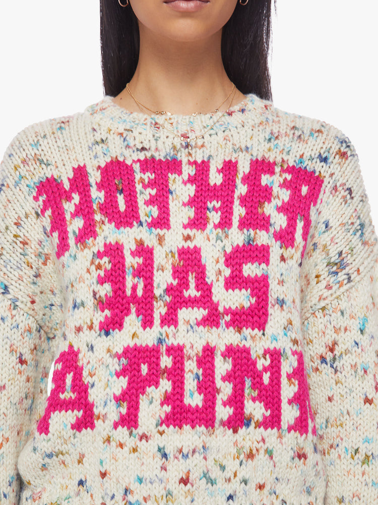 Close up view of a woman crewneck sweater with drop shoulders, long roomy sleeves and a slightly cropped hem in cream with colorful speckles and text in hot pink.