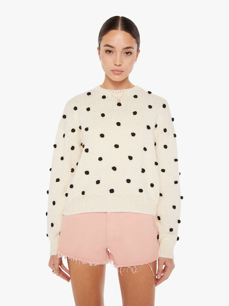 Front view of a womens white knit sweater featuring small black pom poms.