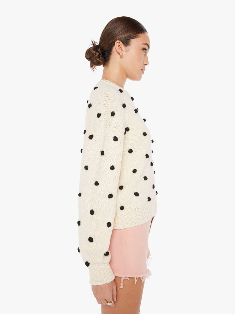 Side view of a womens white knit sweater featuring small black pom poms.