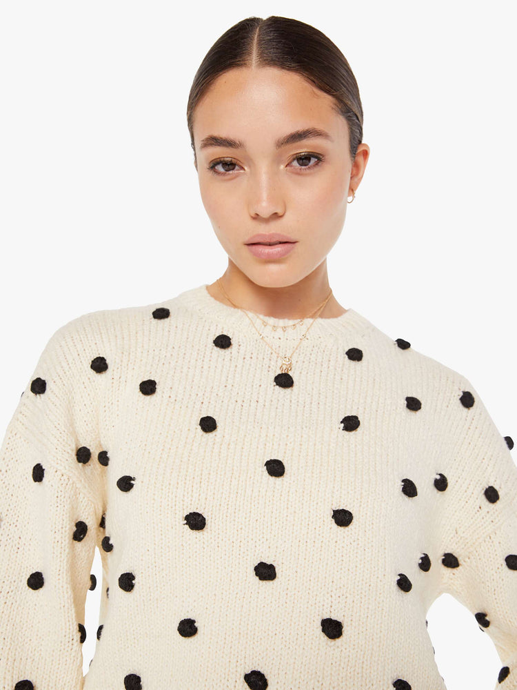 Front close up view of a womens white knit sweater featuring small black pom poms.