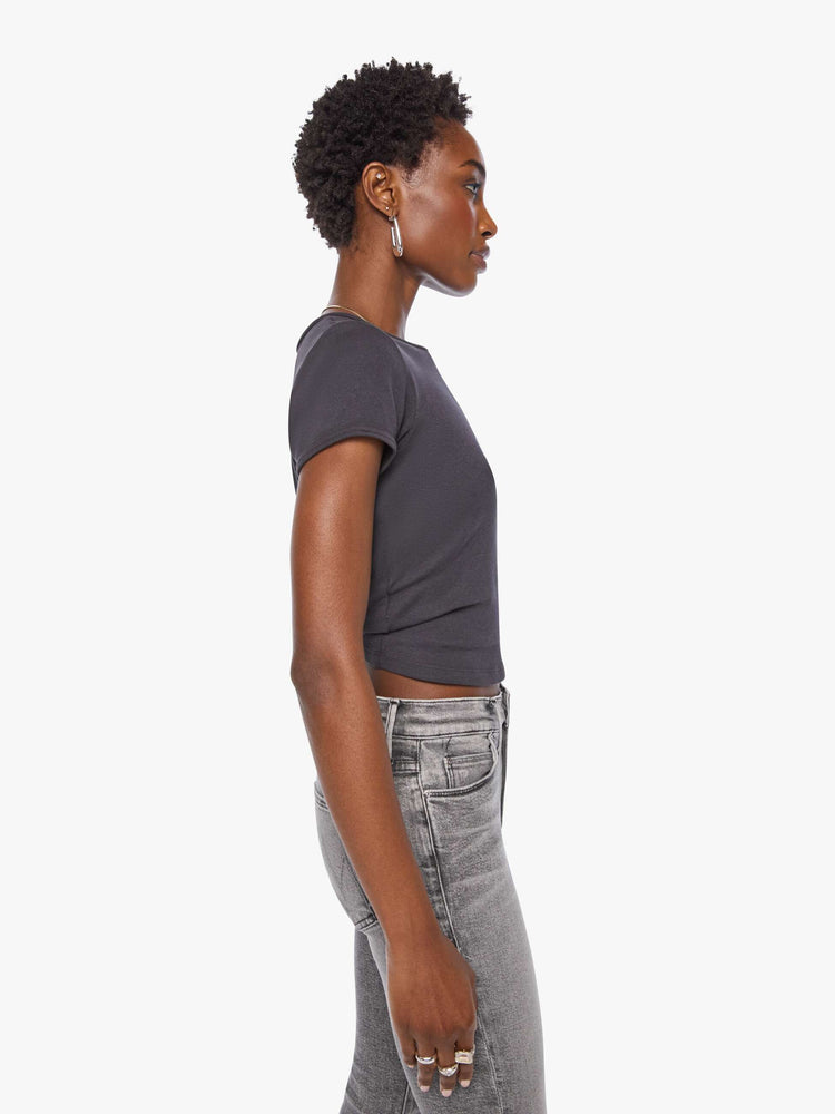 Side view of a woman in a shrunken crewneck tee with extra-short sleeves and a cropped hem in a faded black with a metallic text graphic on the front.