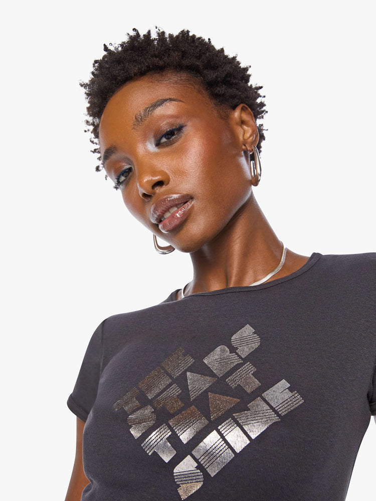 Close up view of a woman in a shrunken crewneck tee with extra-short sleeves and a cropped hem in a faded black with a metallic text graphic on the front.