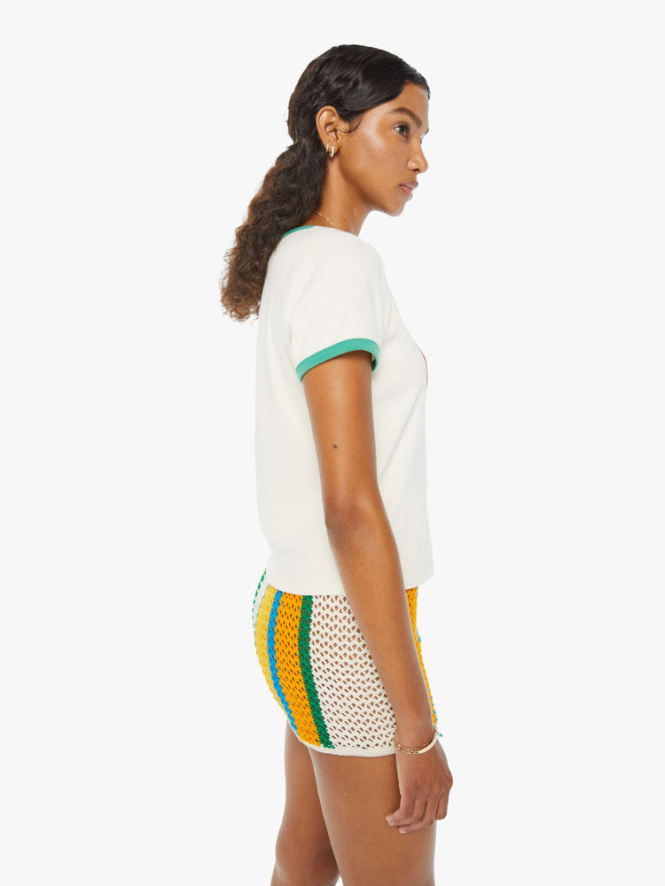 Side view of a woman in an off-white shrunken crewneck tee with extra-short sleeves and a cropped hem designed with a blue whale graphic on the front and teal hems. Paired with crochet shorts.