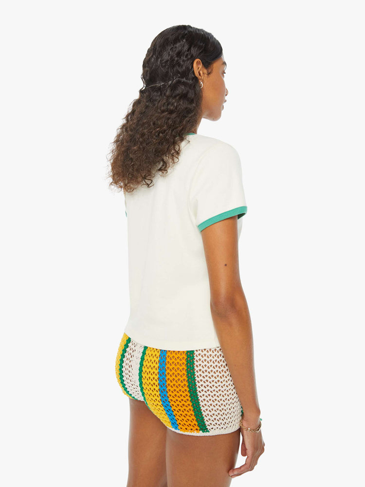 Back view of a woman in an off-white shrunken crewneck tee with extra-short sleeves and a cropped hem designed with a blue whale graphic on the front and teal hems. Paired with crochet shorts. 